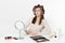 Fun severe woman with curlers on hair sitting at table applying makeup with set facial decorative cosmetics isolated on