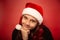 Fun waiting thinking child girl guessing the gift on new year in santa claus hat on red background. Happy Christmas