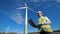 Functioning wind turbine towers and an energetics worker standing beside them with a laptop. Clean, eco-friendly energy