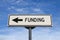 Funding road sign, arrow on blue sky background