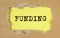 FUNDING word written on yellow table through torn craft paper