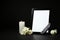 Funeral photo frame with ribbon, white roses and candle on dark table against black background