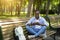 Funky black guy in earphones listening to his favorite music online from cellphone on bench at park, copy space