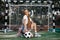 Funky young blonde teenage hipster girl posing with serious face with soccer ball in front of goal post at the stadium