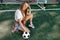 Funky young blonde teenage hipster girl posing with serious face with soccer ball in front of goal post at the stadium