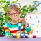 Funny adorable little kid boy with glasses holding watercolors and brushes. Happy child and student is back to school