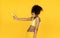 Funny african teen girl hold banana gun shooting isolated on yellow background