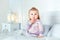 Funny amazed blond little girl sitting on bed in bedroom