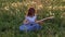 Funny attractive little girl sits in the grass and plays the jeans guitar. field with dandelions in spring bloom at sunset. concep