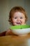 Funny baby eating food himself with a spoon on kitchen. Smiling baby eating food. Funny child face closeup. Launching