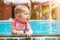 Funny baby under one year old looks out of the pool with interest, looks to the right. Sunny day, summer vacation