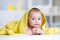 Funny baby under soft towel. Cute child lying on bed after bathing in living room