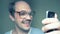 Funny balding man in glasses uses a smartphone and smiles