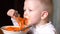 Funny blond boy is eating Korean carrot salad in kitchen next to his brother. Children are happy together