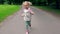 Funny blond girl with pigtails running through park road in front of camera