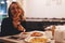 Funny blonde girl in black sweater with hood eating pizza at restaurant.