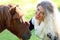 Funny blonde girl strokes chestnut pony muzzle, sunny day