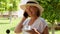 funny blonde senora woman, 50-55 years old, in a hat and a white dress, talks using a smartphone and holds a cup of