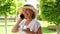 funny blonde senora woman, 50-55 years old, in a hat and a white dress, talks using a smartphone and holds a cup of