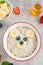Funny bowl with oat porridge with bear faces made of fruits and berries on a gray concrete background. Food for kids idea