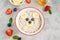 Funny bowl with oat porridge with bear faces made of fruits and berries on a gray concrete background. Food for kids idea
