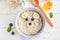 Funny bowl with oat porridge with bear faces made of fruits and berries on a white wooden background. Food for kids idea, top view