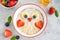 Funny bowl with oat porridge with owl faces made of fruits and berries on a gray concrete background. Food for kids idea, top view