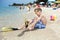 Funny boy diver sitting on sandy beach putting on diver flippers