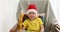 Funny boy in red white Christmas hat sits on chair smiling