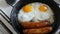 Funny breakfast in the pan in the form of a face and a smile with eyes. Two fried eggs and thick Bavarian sausages fried