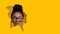 Funny cheerful young african american lady in glasses holds pencil with lips and nose, looks into hole in yellow paper