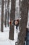 Funny child boy hides behind tree in winter forest. Boy is dressed in warm hat and winter jumpsuit. Vertical frame