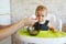 Funny child girl eating from the spoon. Woman feeding little baby sitting in baby chair in the kitchen