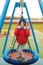 Funny child having fun with modern swing. Little boy playing on outdoor playground. Happy kid swinging on cold autumn day. Active