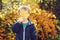 Funny child hide his face behind a maple leaf. Cute little boy playing with fallen leaves in city park. Autumn time. Autumn kids f