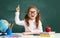 Funny child   schoolgirl    student  raises his hand up near school blackboard