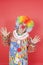 Funny clown with arms raised looking away against colored background