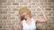 Funny comic blonde girl with fluttering curly short hair, brick wall background. copy space. Emotion concept, joy fun