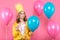 Funny conceptual photography. Cheeky girl in birthday hat holding needle pretending to pop birthday balloons. Celebrating birthday