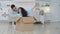 Funny curly haired lady sitting inside carton box. Hispanic man pushing parcel with woman. Happy couple renters buyers