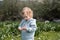 Funny cute adorable caucasian blonde baby girl, toddler in green field of daisy, camomiles gathering flowers.Curious