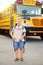 Funny cute happy Caucasian boy student kid near yellow bus. Back to school concept