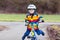 Funny cute preschool kid boy in safety helmet and colorful raincoat riding his first bike