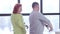 Funny dance of cheerful adult Caucasian couple indoors. Positive carefree relaxed man and woman dancing at window in