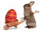 Funny Easter bunny rabbit with a wheelbarrow and a red Easter egg