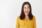 Funny and emotive young woman, showing tongue and winking happy at camera, standing in yellow blouse on white background