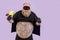 Funny evil obese man in carnival costume holds toy blaster posing on purple background