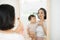 Funny family at home. Mother and her child girl are doing your makeup and having fun near mirror. Baby girl explores mother`s