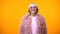 Funny fashionable aged lady in pink coat and round sunglasses smiling on camera