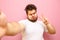 Funny fat man with beard takes selfie on pink background and shows funny face. Charismatic young overweight man shows funny facial